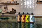 Four Motif syrup squeeze bottles arranged on a glossy green tiled counter, featuring Chocolate, Cinnamon Babka, Pistachio, and Vanilla flavors.
