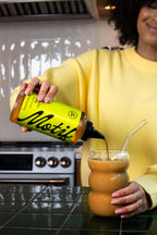 Woman in a yellow sweater pouring Pistachio Syrup into an iced coffee using the bottle's precision cap.