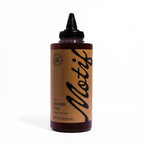 Bottle of Motif Premium Chocolate Syrup with a chocolate brown label and black twist precision cap.